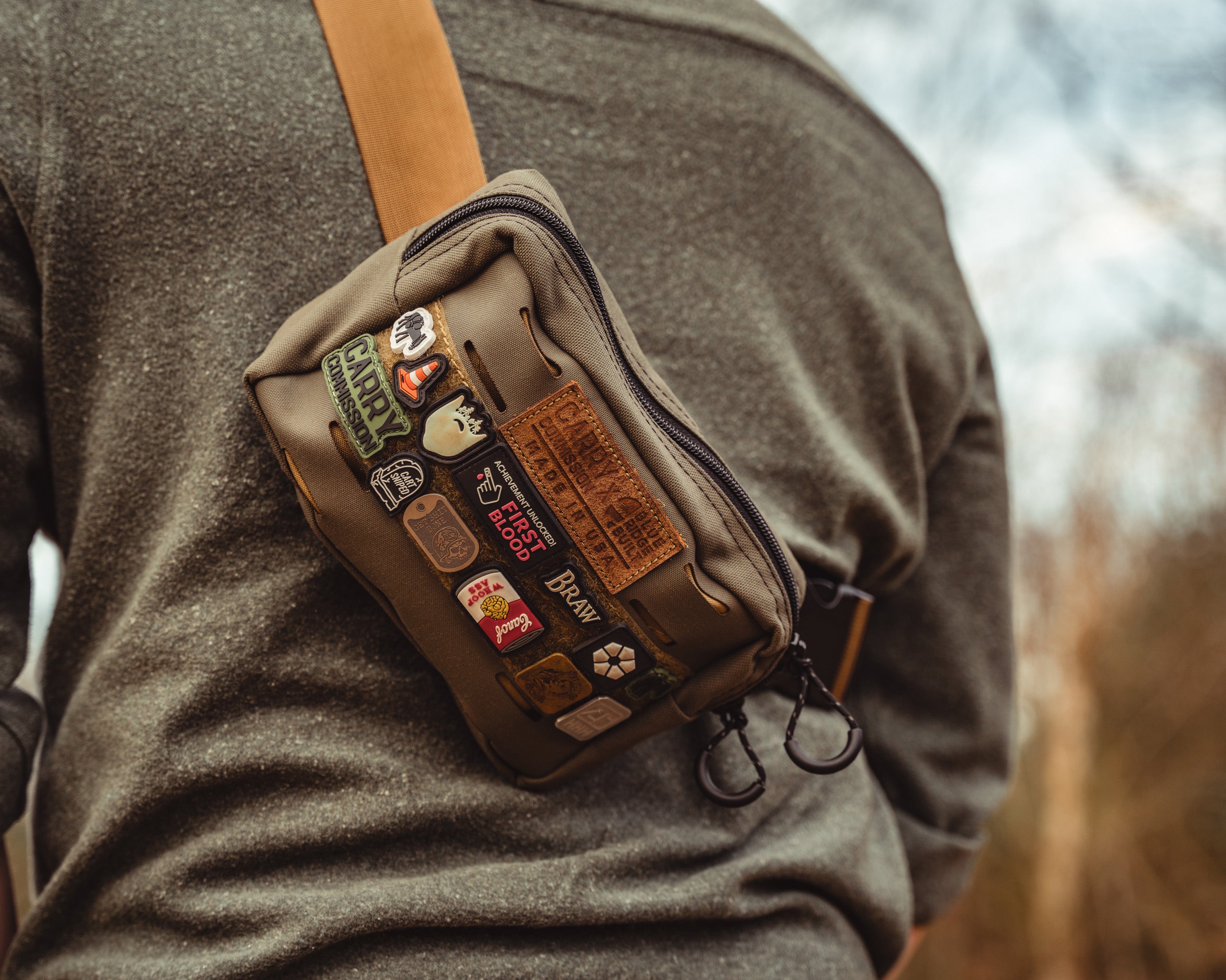 Carry Commission / Blue Ridge Overland Gear Bum Bag XL close up view being modeled as an over the shoulder sling with lots of ranger eye patches on the front hook and loop strip