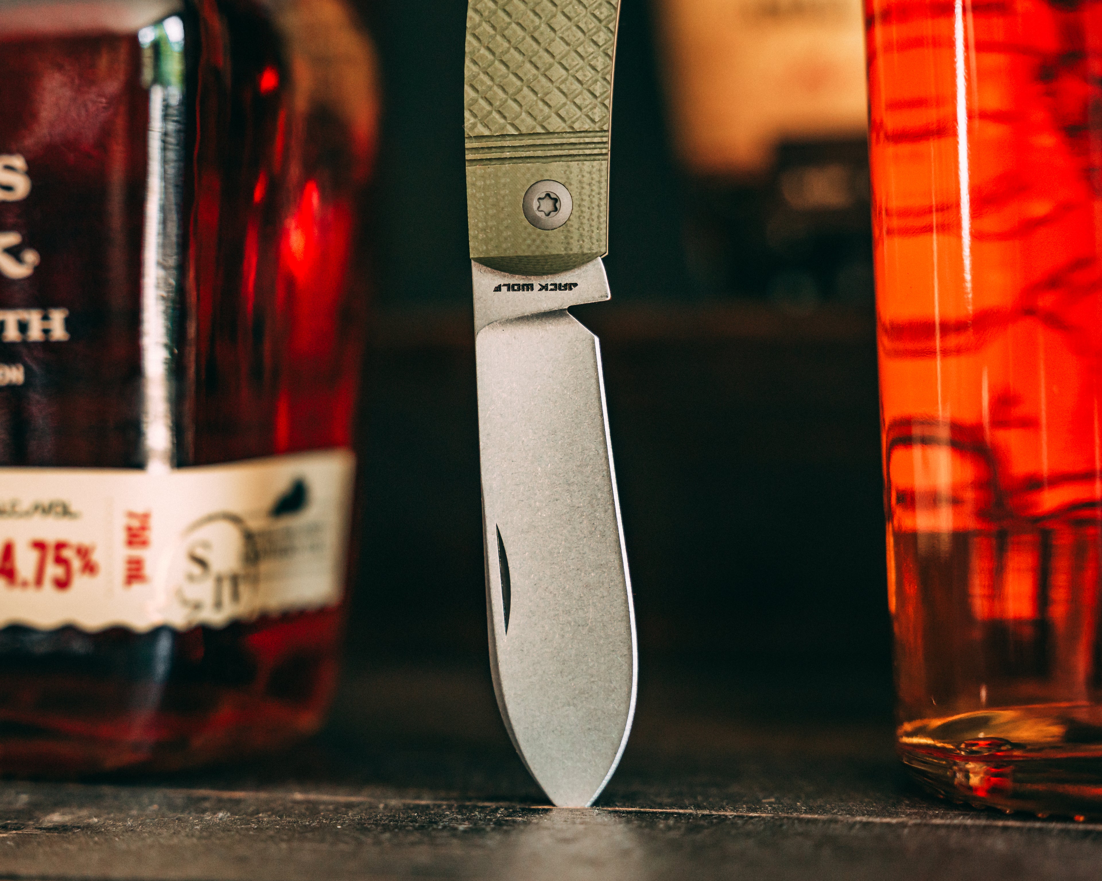 Knife with a green handle next to a bottle of Stoli Vodka on a dark surface.