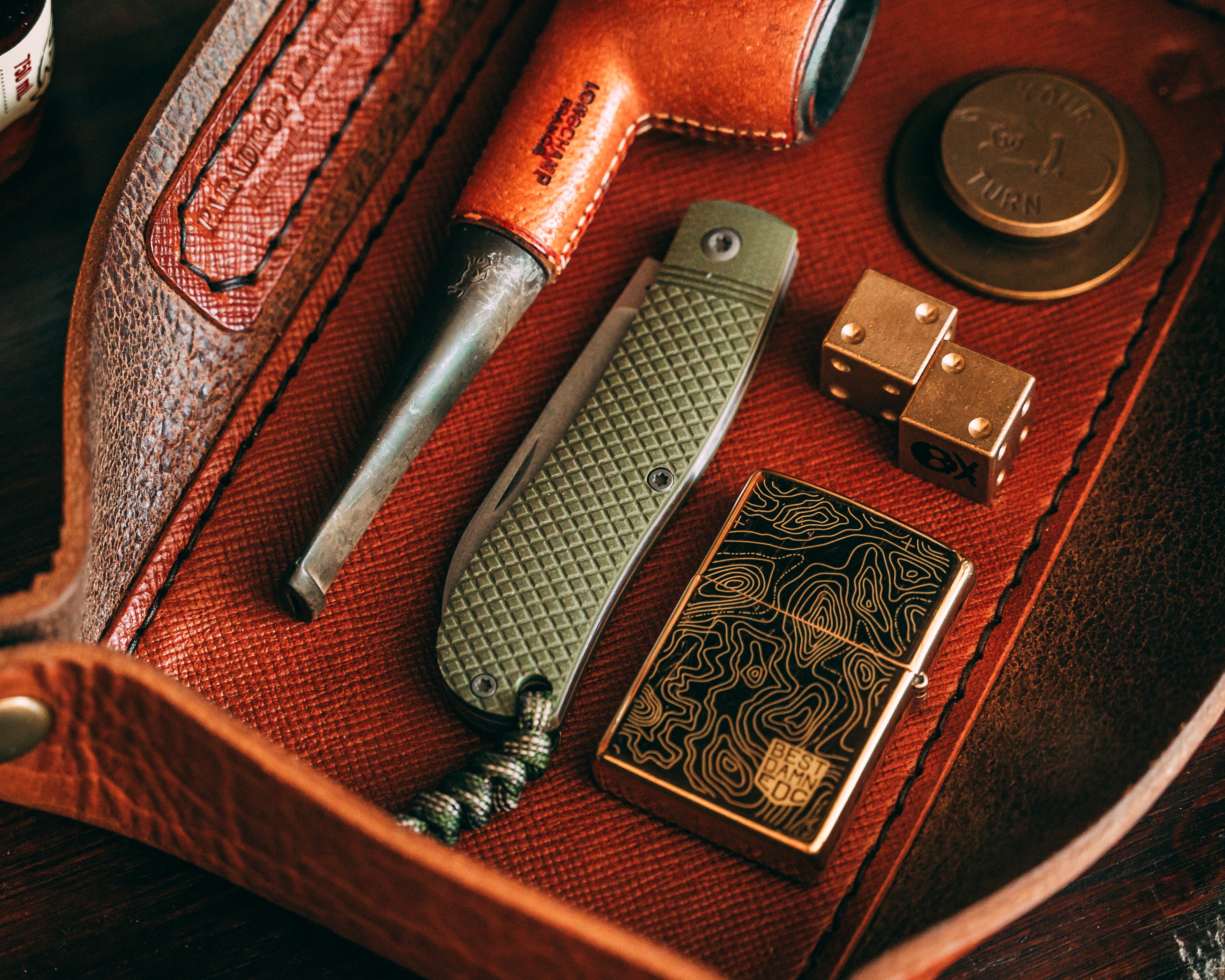 Close-up of a leather case with a knife, pipe, and Zippo lighter.