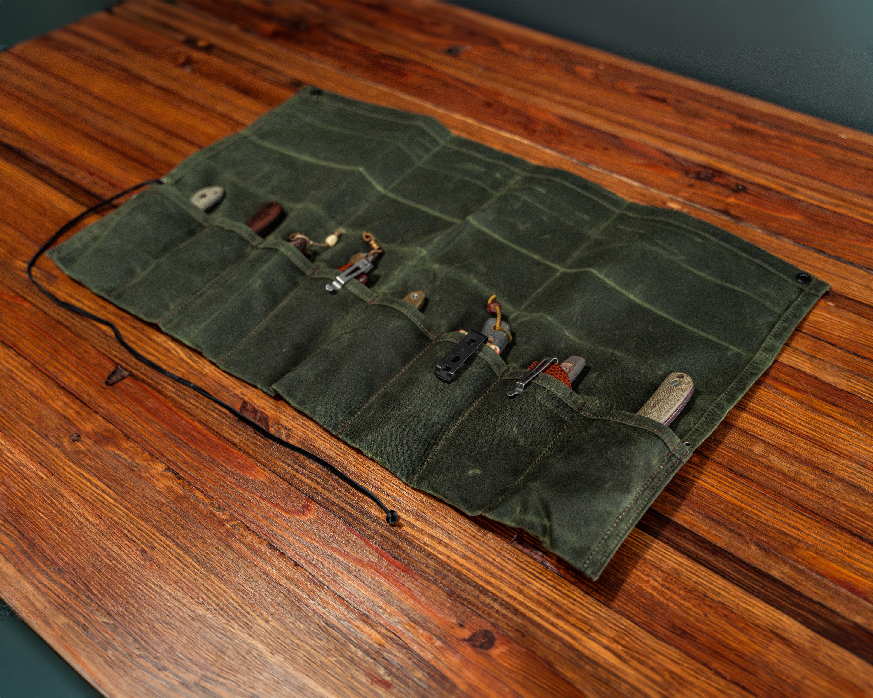 Zoomed out view of the open Birch Waxed Canvas Knife Roll with knives inside of it on a wooden surface