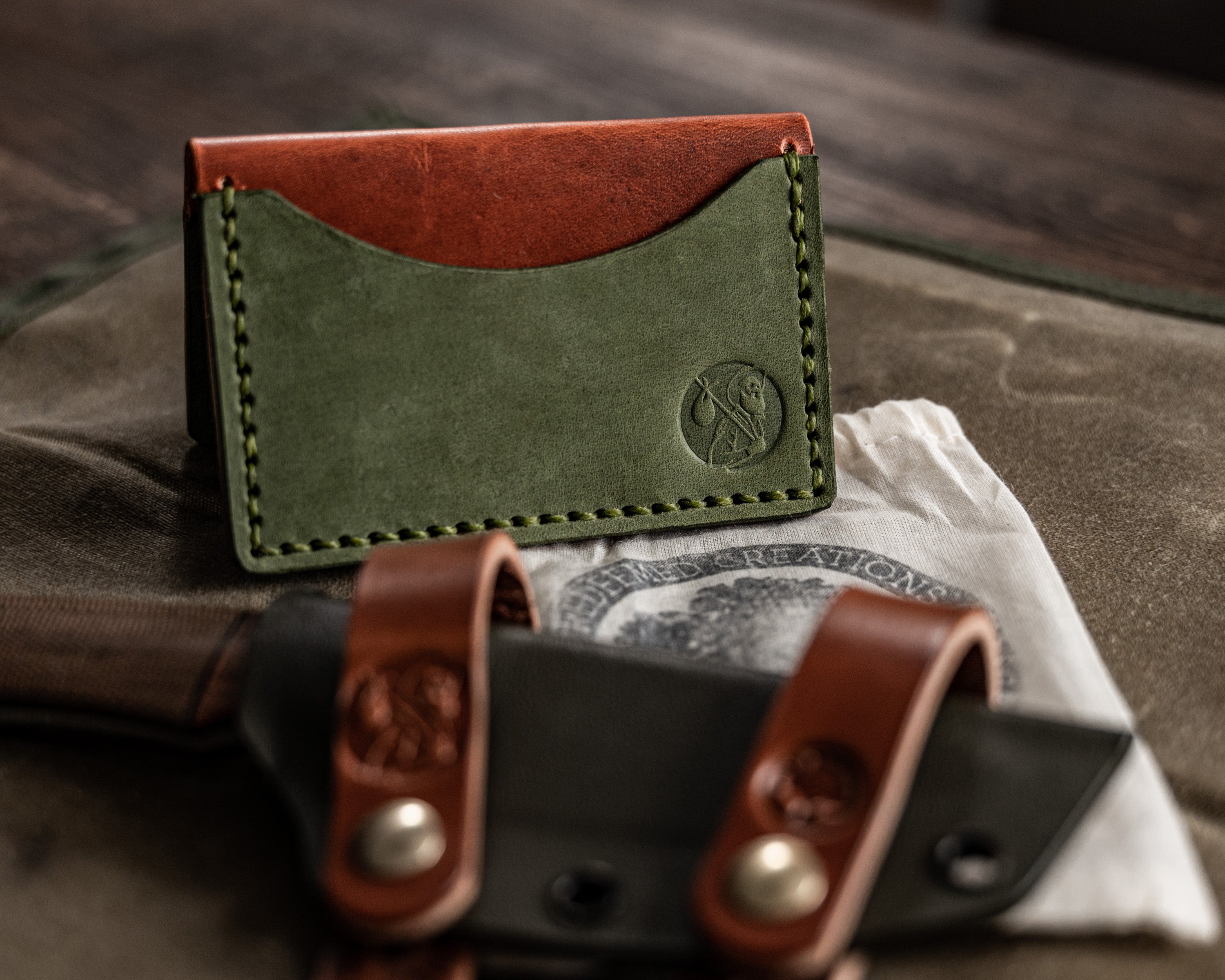 Top view of a brown and green bifold wallet in a "tent" shape on top of a canvas tray with a sheath and cloth bag also in photo