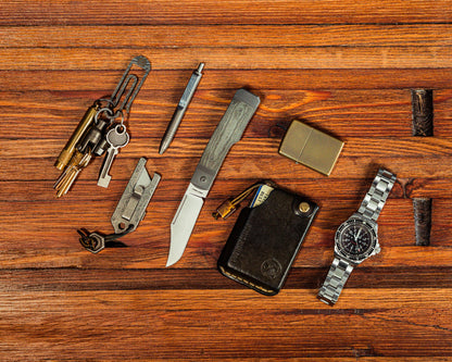 Gunslinger Jack Knife flay lay on wooden surface surrounded by EDC items like wallet, watch, pen, keychain, tpt slide and lighter