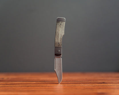 Gunslinger Jack Knife standing upside down on wooden surface with tip piercing wood