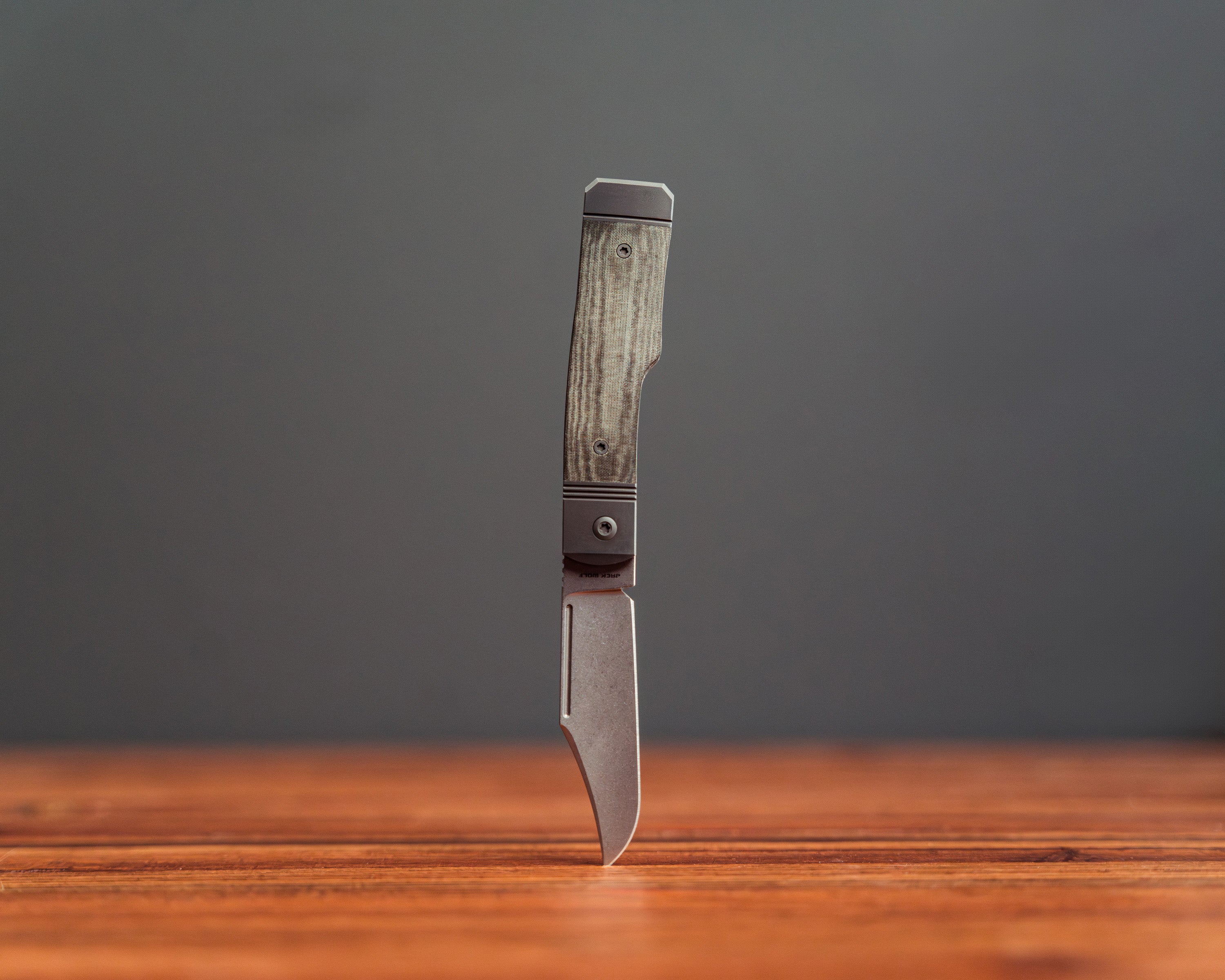 Gunslinger Jack Knife standing upside down on wooden surface with tip piercing wood