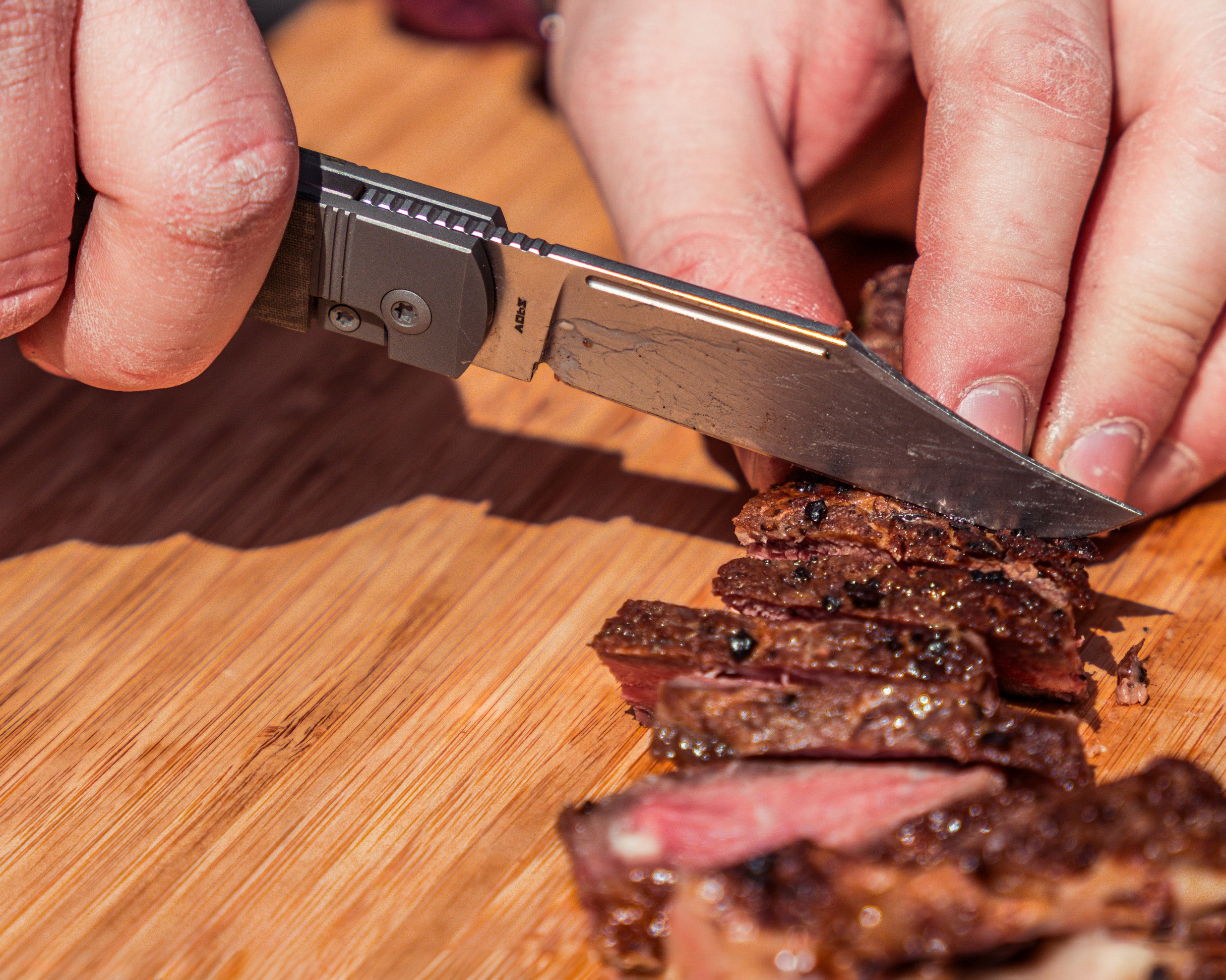 Gunslinger Jack Knife slicing through steak on a wooden cutting board