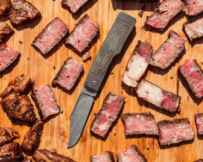 Gunslinger Jack Knife flat lay on cutting board surrounded by pieces of cut up steak
