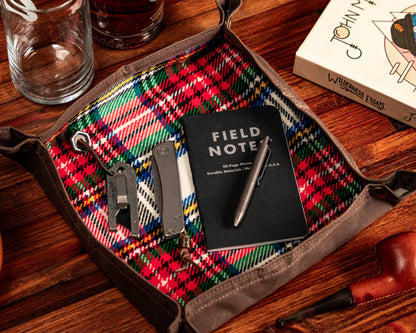 Carry Commission / PNW Bushcraft Vintage Plaid Waxed Canvas Travel Tray zoomed in overhead view with note pad, pen, knife and TPT Slide contained inside against a wooden background.