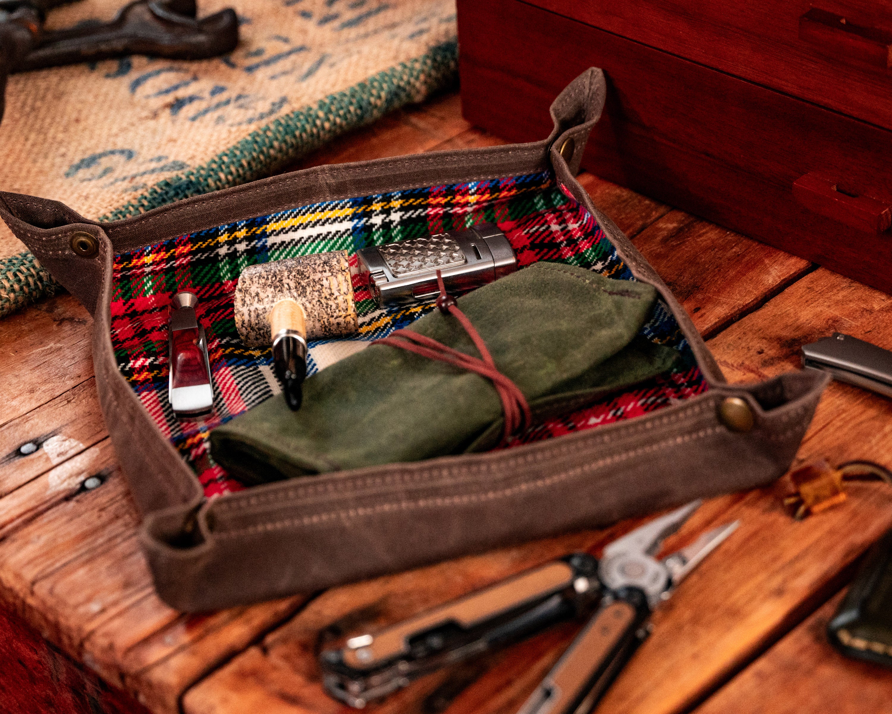 Carry Commission / PNW Bushcraft Vintage Plaid Waxed Canvas Travel Tray sideways view with a smoking pipe and accessories sitting on a wooden surface.