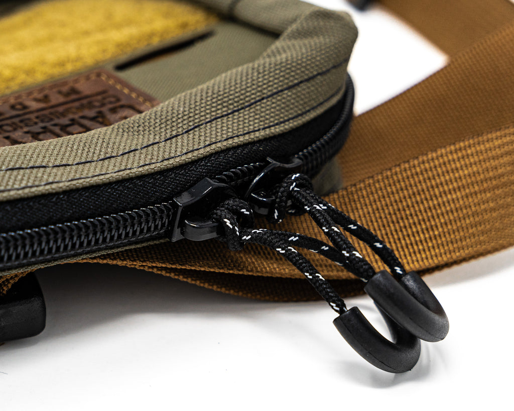 Close up of black zipper and zipper pulls attached to the  Bum Bag in green and tan color way with leather patch logo