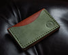 Top view of the back of a bifold brown and green wallet on black leather background