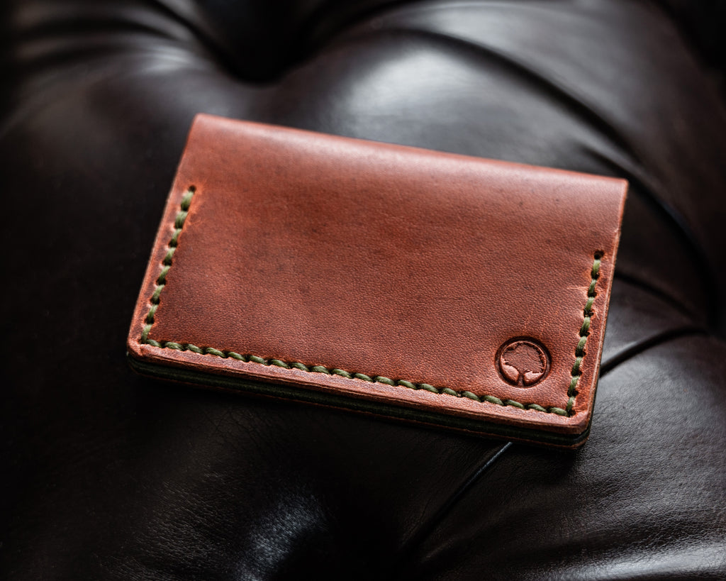 View of the front of a bifold brown and green wallet on black leather background