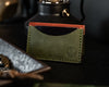 Backside view of brown and green bifold wallet in a "tent" shape on a black table with an edc tray in foreground and lamp in background
