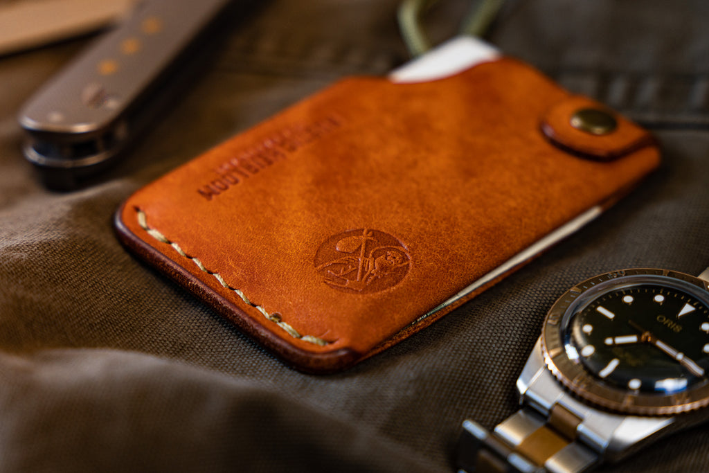 Front side of Rustic Heirloom's Carry Commission  Hitchhiker Wallet in leather with olive drab thread and paracord on cloth background with watch in foreground.