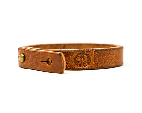 Carry Commission and Rustic Heirloom leather Wrist Strap laid on its side showcasing the Carry Commission Logo of the man holding a bindle.