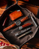 Overhead view of Rustic Heirloom's Carry Commission  Hitchhiker Wallet in leather with olive drab thread and paracord placed in dump tray with leather banded watch, CWF Flashlight, Carry Commission Vero Pry, pen, and folding knife.