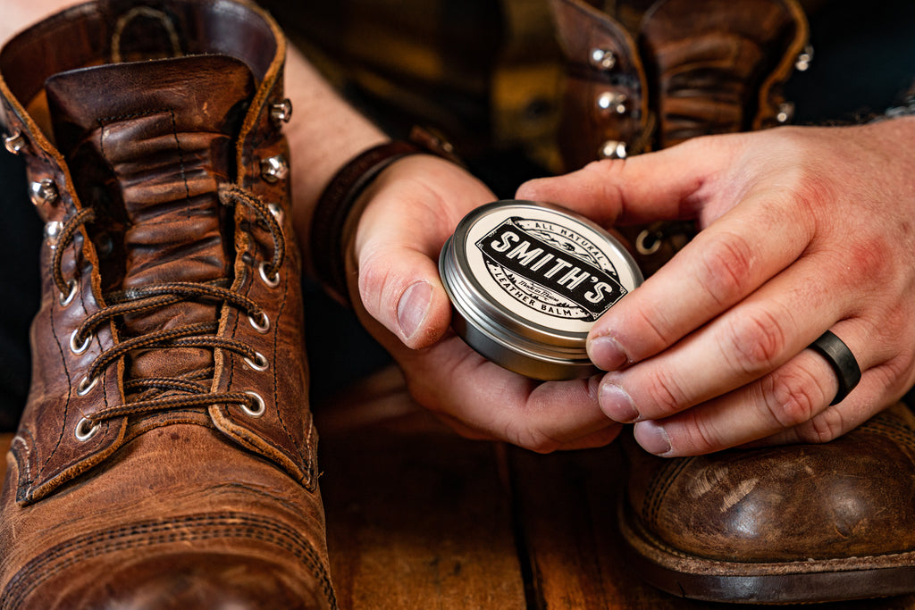 Pair of hands holding Smith's Leather Balm Tin around a pair of leather boots.
