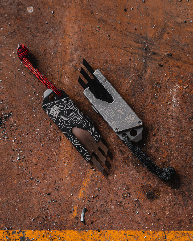 Overhead view of Best Damn EDC TPT Slide Box Cutter Tool in Black & Stonewash Topo on rust background.