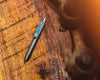 Titanium Carry Commission & Big Idea Design mini click pen sitting on a wooden surface