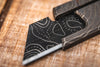 Close up of the Topo ZeroFeud Fauxmascus Blade in a box cutter on a wooden background