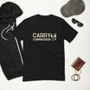 Front side of black Carry Commission T-shirt sporting the lettering and man holding bindle on shoulder set on a white background with a hoodie, sunglasses, baseball cap and wallet placed around shirt.