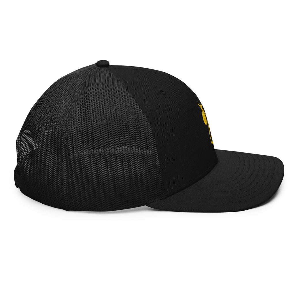 Left side view of black trucker cap with Carry Commission logo of man holding bindle on shoulder in gold. 